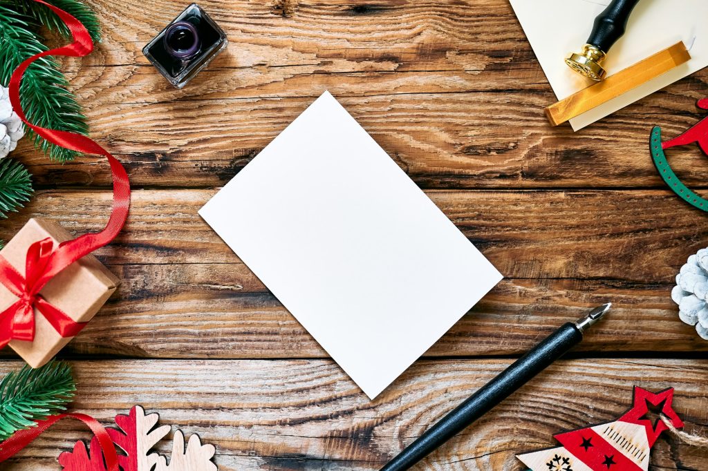 Mail envelope and paper sheet with fountain pen and inkwell on wooden table with Christmas decor.