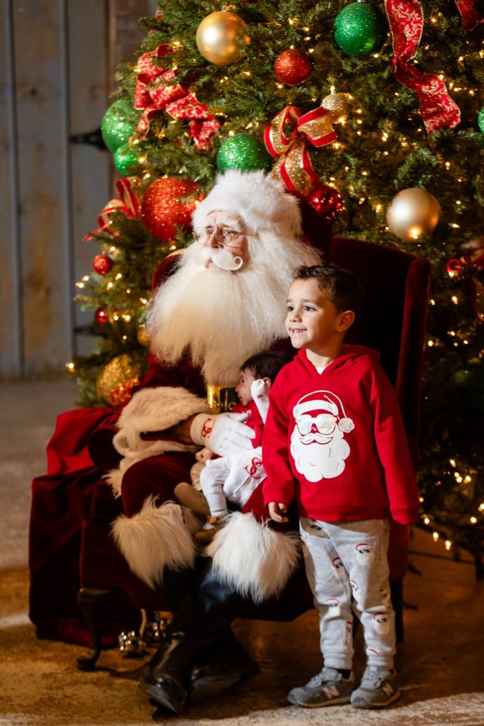 Smiling boy in a Santa sweater posing with Santa Claus at Old West Christmas Light Fest