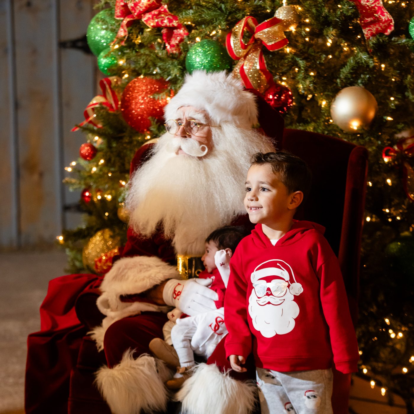 Smiling boy in a Santa sweater posing with Santa Claus at Old West Christmas Light Fest