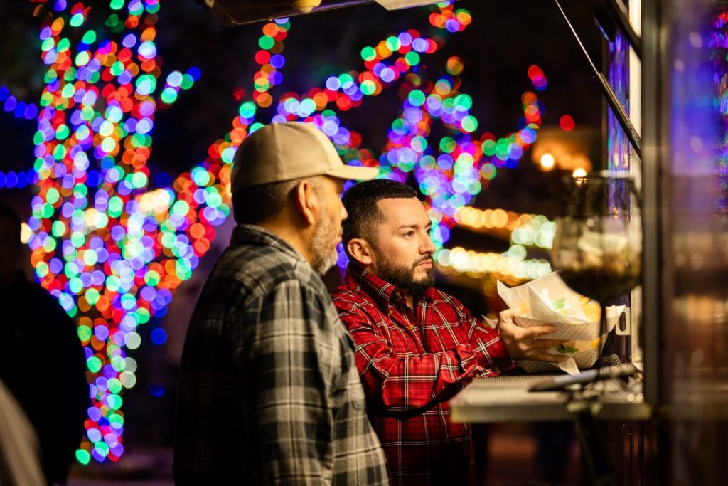 A guest picking up a food order under the Christmas lights at Old West Christmas Light Fest